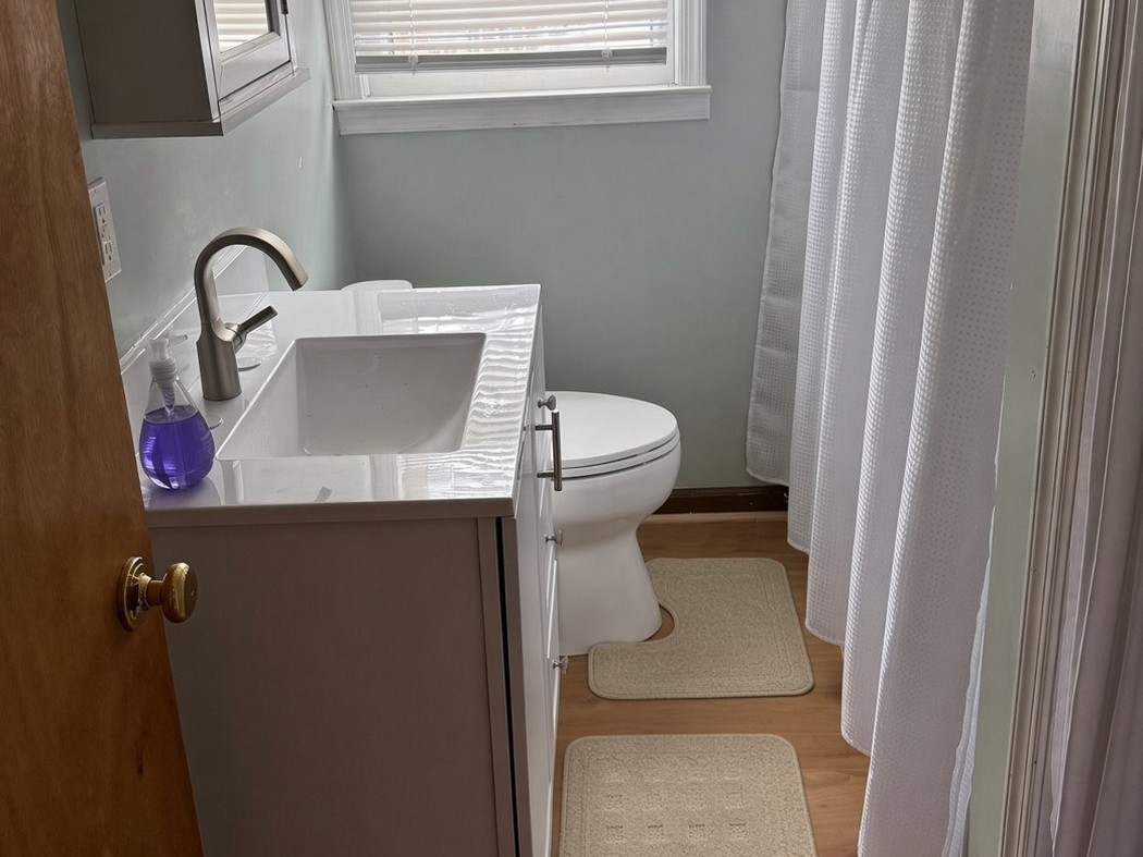 Remodeled bathroom with white shaker vanity, new fixtures and plank flooring
